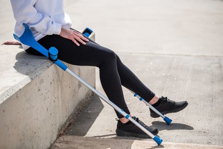 person sitting on cement wall with crutches