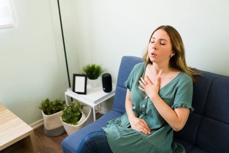 women sitting on couch breathing with hand on chest and lap
