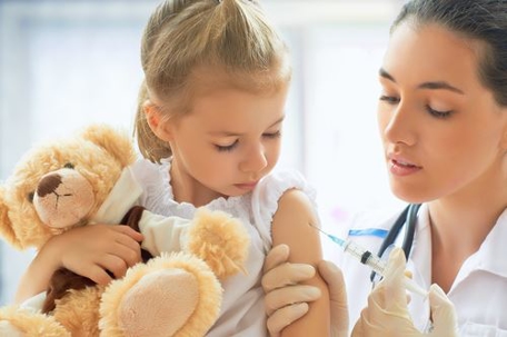 little girl holding teddy bear while doctor gives her a shot